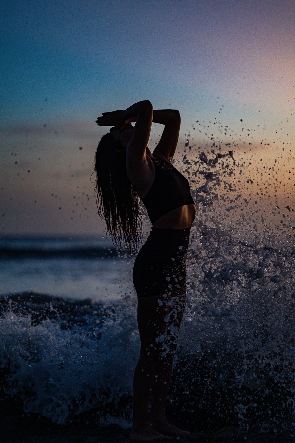 Silhouette of a dancer against ocean waves and sunset sky creating a dramatic splash effect.
