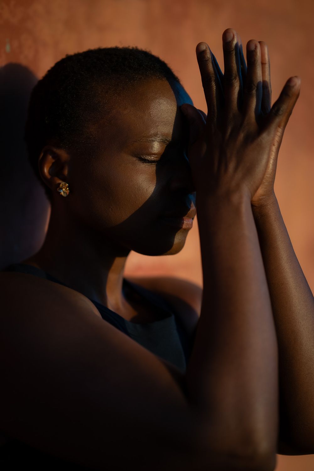 Intimate portrait with hands pressed together in prayer position against warm-toned background.