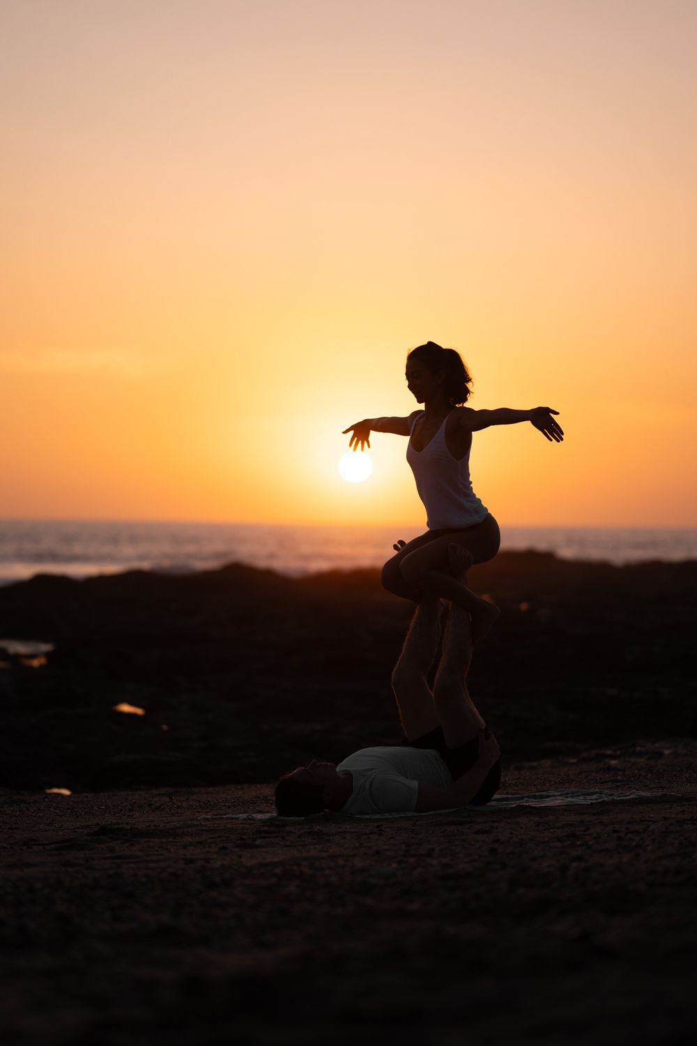 Silhouette of person jumping with arms spread against vibrant orange beach sunset.