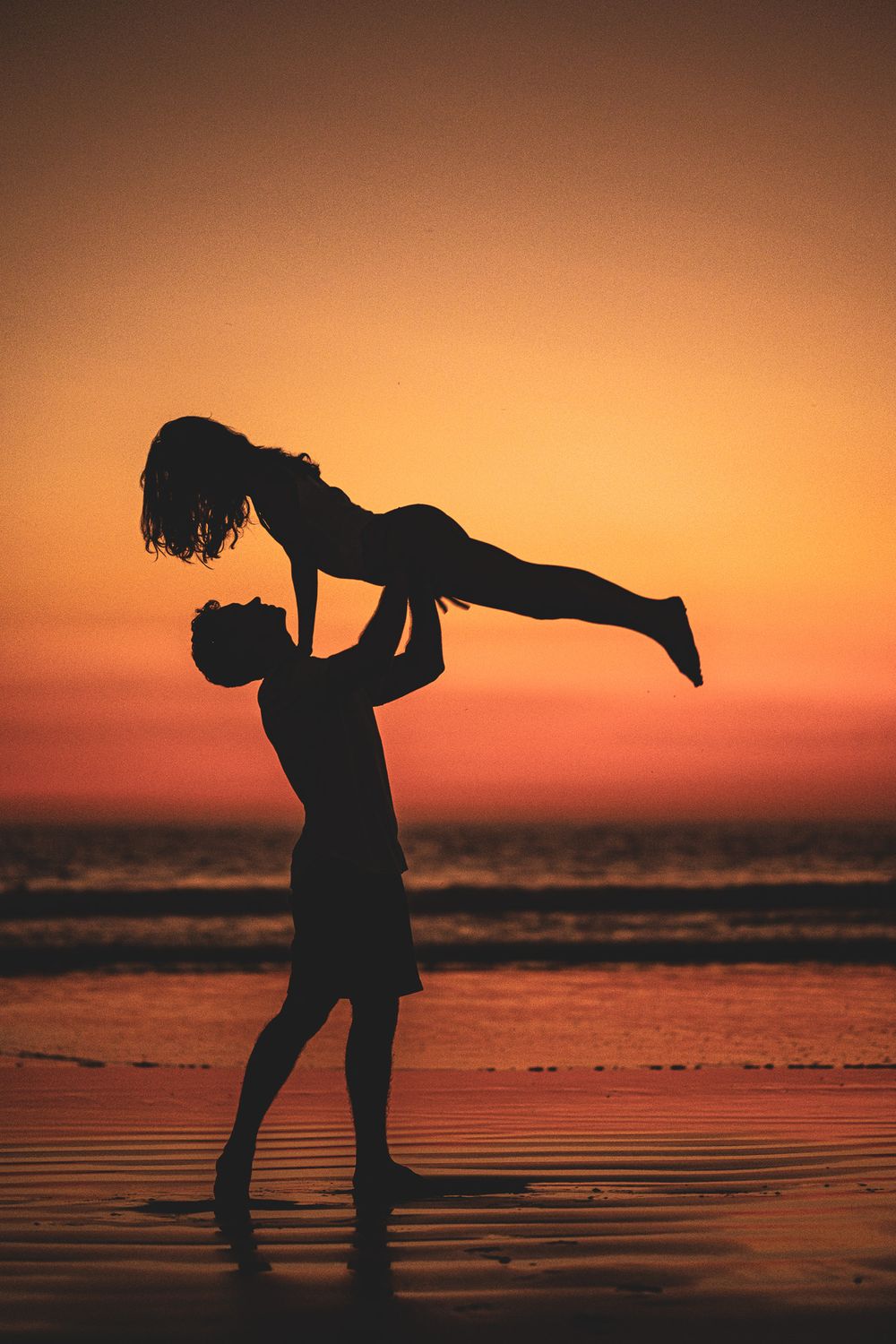 Couple doing accro yoga at the beach together during a sunset photoshoot for their personal branding in yoga