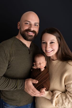 Professional studio family portrait with a sleeping newborn baby against a dark background.