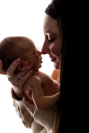 Silhouetted tender moment between parent and baby in soft lighting with gentle touching of faces.