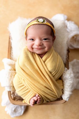 Newborn wrapped in soft yellow swaddle blanket resting in wooden basket with white fabric. NJ newborn photographer