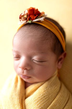 Sleeping newborn wrapped in soft yellow swaddle wearing mustard headband with autumn floral accents. NJ newborn photographer