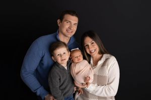 A happy family of four poses together against a black backdrop in a warm studio portrait.