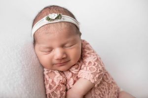 Sleeping newborn in pink lace outfit wearing delicate floral headband.