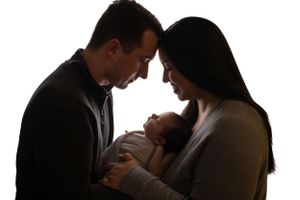Silhouette of parents looking lovingly at their newborn baby against white backdrop.