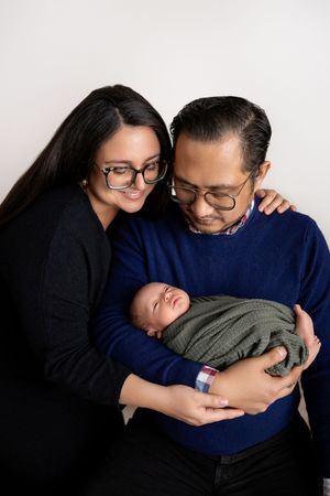 A tender series of images showing a couple holding and gazing lovingly at their newborn baby against a white backdrop.