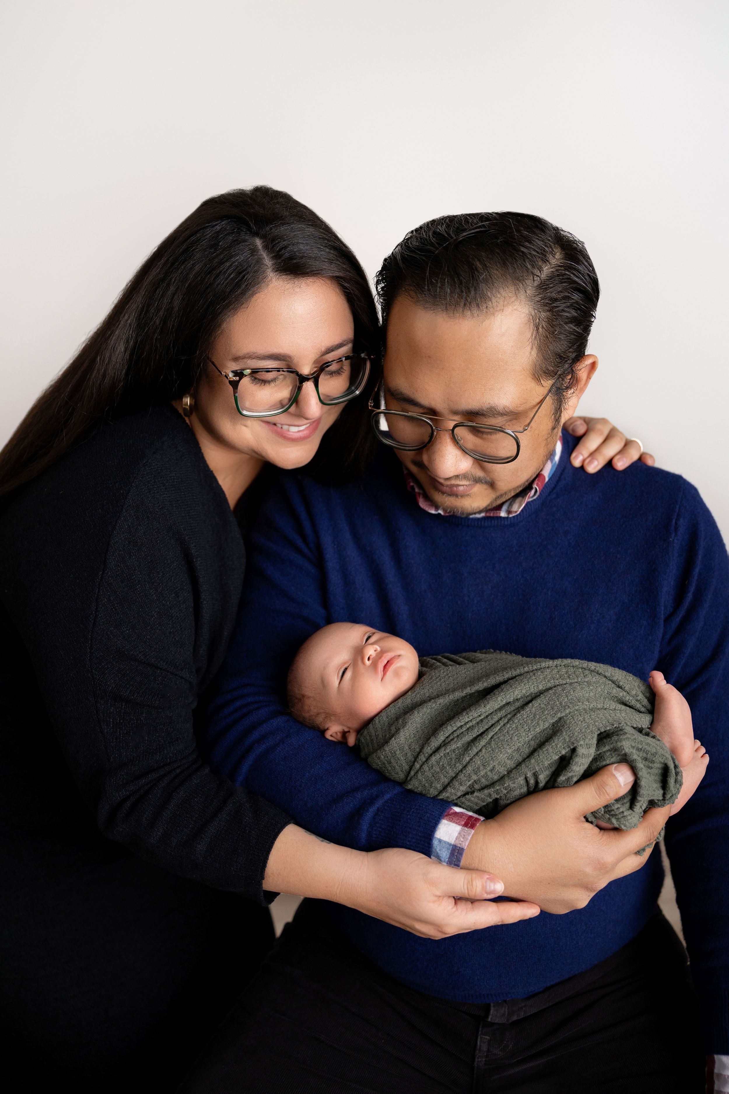 A tender series of images showing a couple holding and gazing lovingly at their newborn baby against a white backdrop.