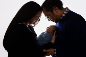 Parents gazing lovingly at their newborn baby in dramatic silhouetted portrait.
