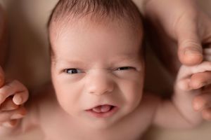 Close up portrait of a newborn baby with rosy cheeks and tiny hands visible in soft lighting.