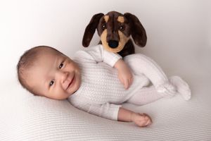 Professional newborn photography session with baby posed on white textured blanket.