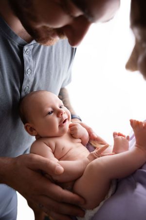Gentle hands cradle a newborn baby in a gray shirt against a white background during an intimate photography session.