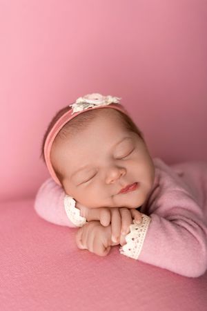 A sleeping newborn baby swaddled in pink blankets rests peacefully on a soft pink background.