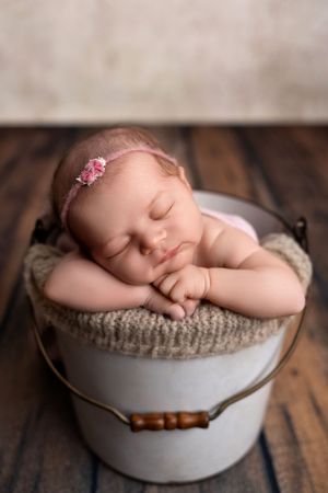 A sleeping newborn rests peacefully in a white bowl with knitted fabric on a rustic wooden surface.