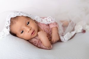 A baby wearing lace lies on a gray textured blanket in a soft, dreamy pose.