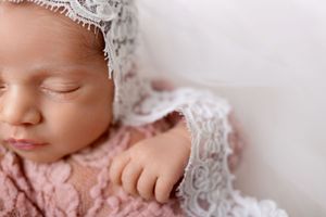 Close up of a sleeping newborn baby wearing delicate lace in soft pink tones.