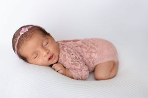Peaceful newborn baby sleeping in pink lace outfit on white background during professional photo session.