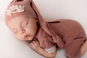 A baby in a cozy pink knit outfit sleeps peacefully on soft fabric.