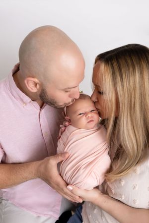 A series of tender family moments captured in soft pink tones showing parents kissing their newborn baby.