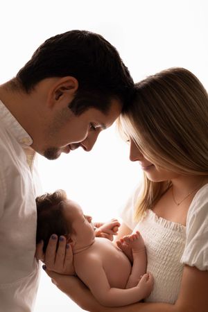 A couple gazes lovingly at their newborn baby in an intimate backlit portrait.