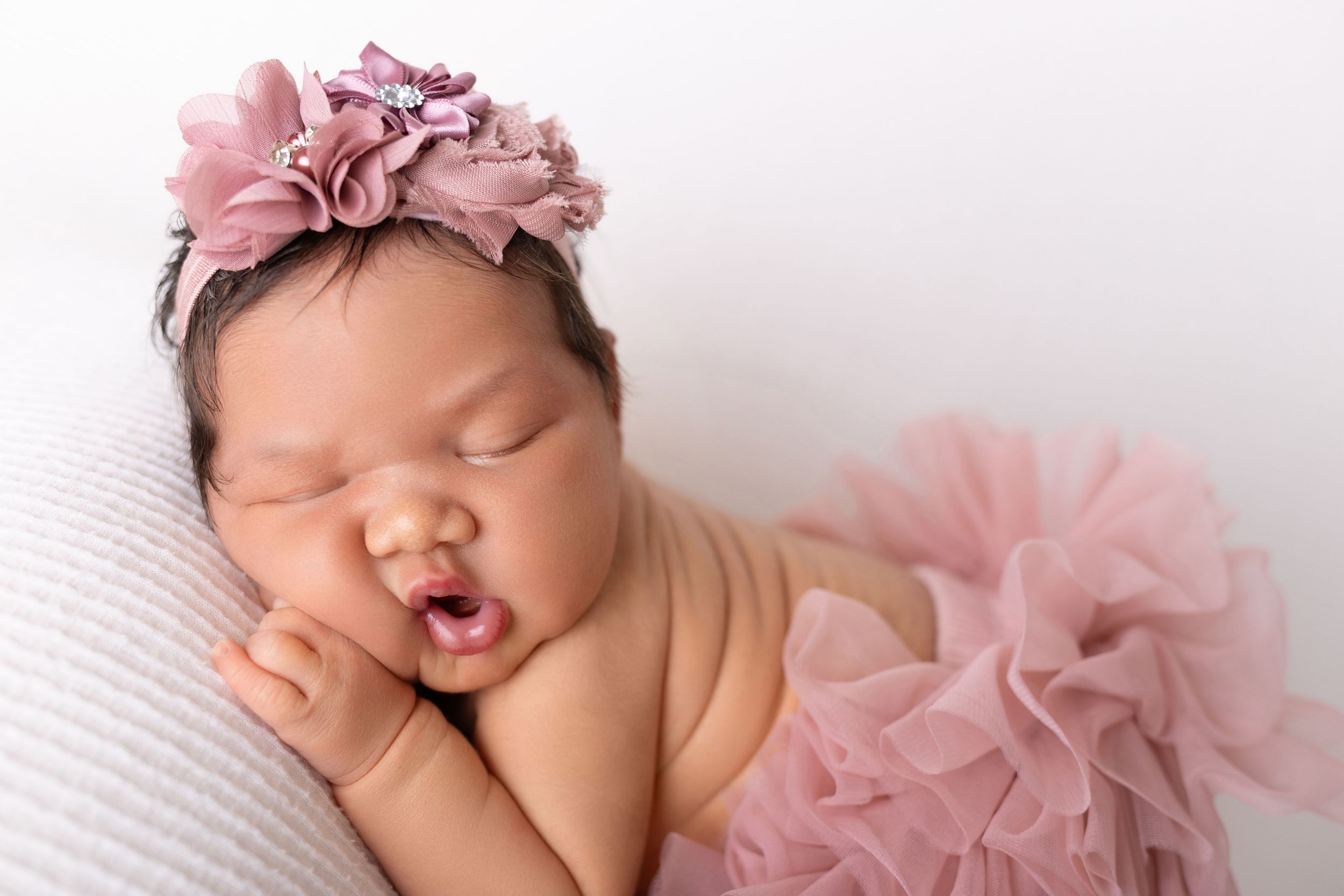 Sleeping newborn baby wearing pink tulle skirt rests peacefully on white blanket during professional photo session.