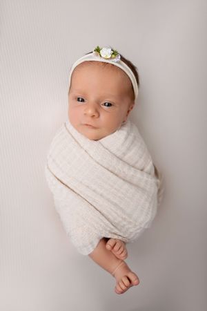 A series of four professional newborn photos showing a baby swaddled in white fabric against a light gray background.