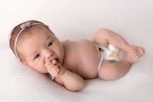 A sleeping newborn baby lies peacefully on soft white fabric in a minimalist photography setting.