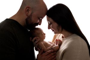 Silhouetted family sharing an intimate moment with their baby in warm backlit setting.