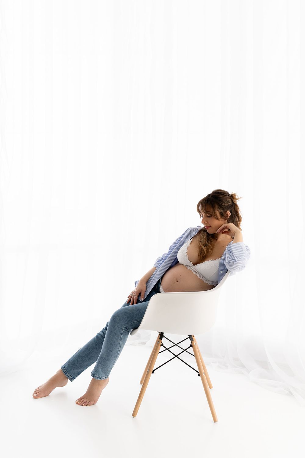 A woman in jeans and button-up shirt lounging in a modern white Eames chair.