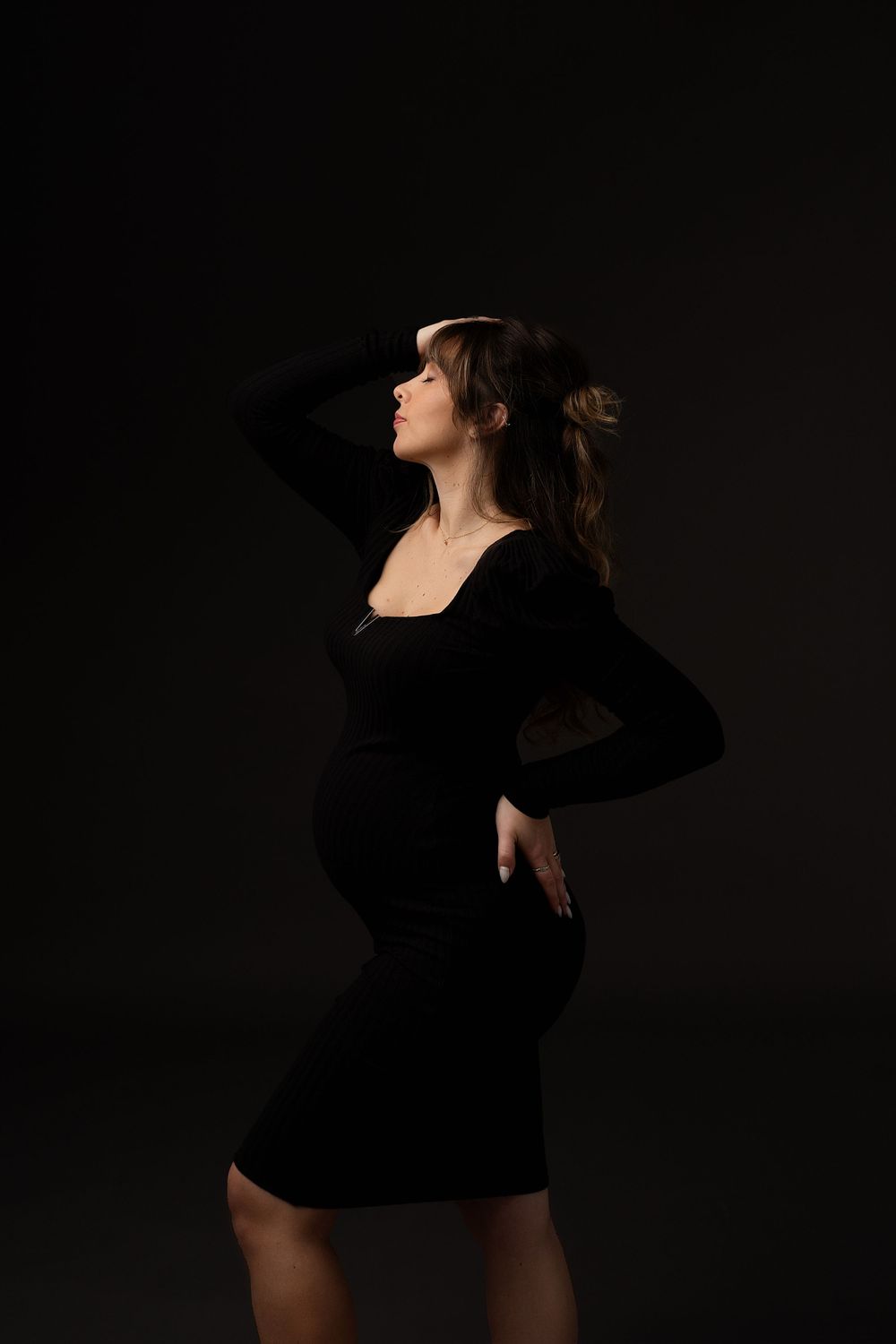 A silhouette of a pregnant woman in black dress against dark background.