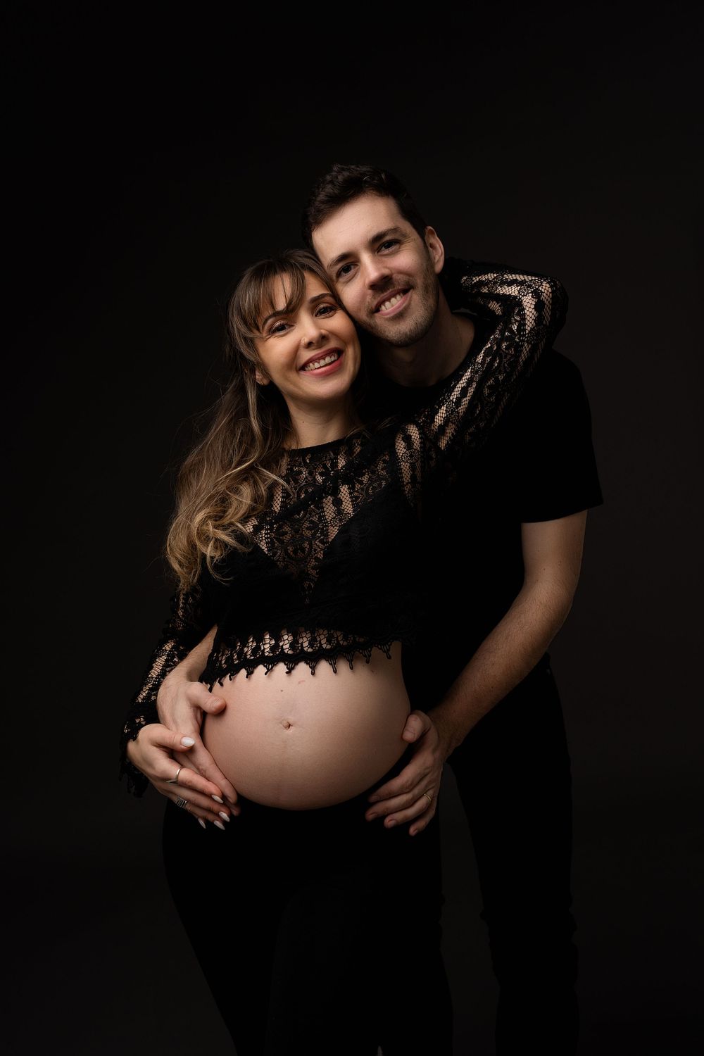 A maternity photo showing a couple in black clothing against a dark background.