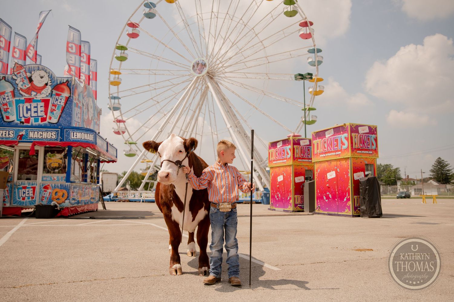 Show animal and handler stand near ferris wheel and carnival food stands at county fair.