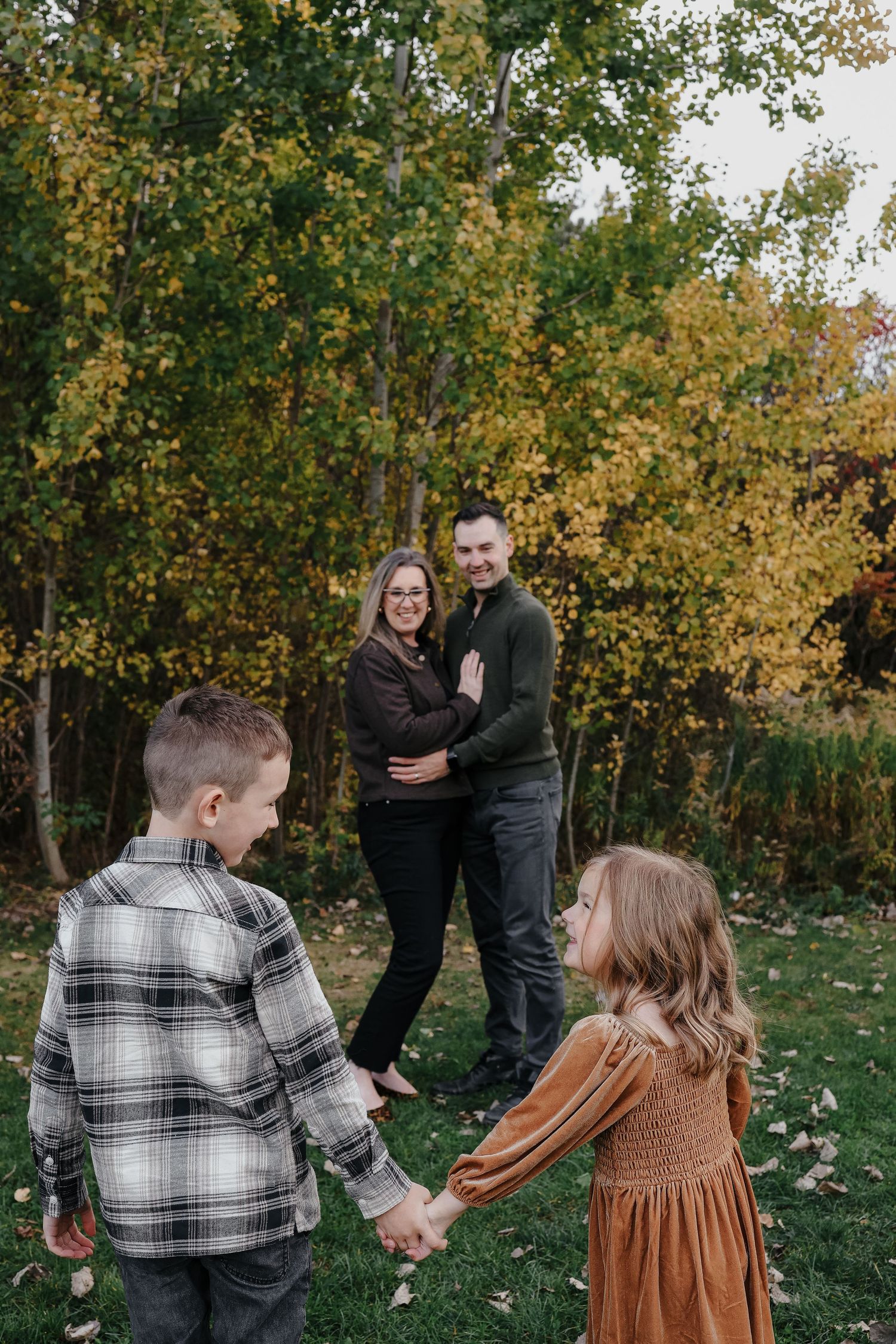 Family embracing outdoors with fall foliage in the background on an overcast day.
