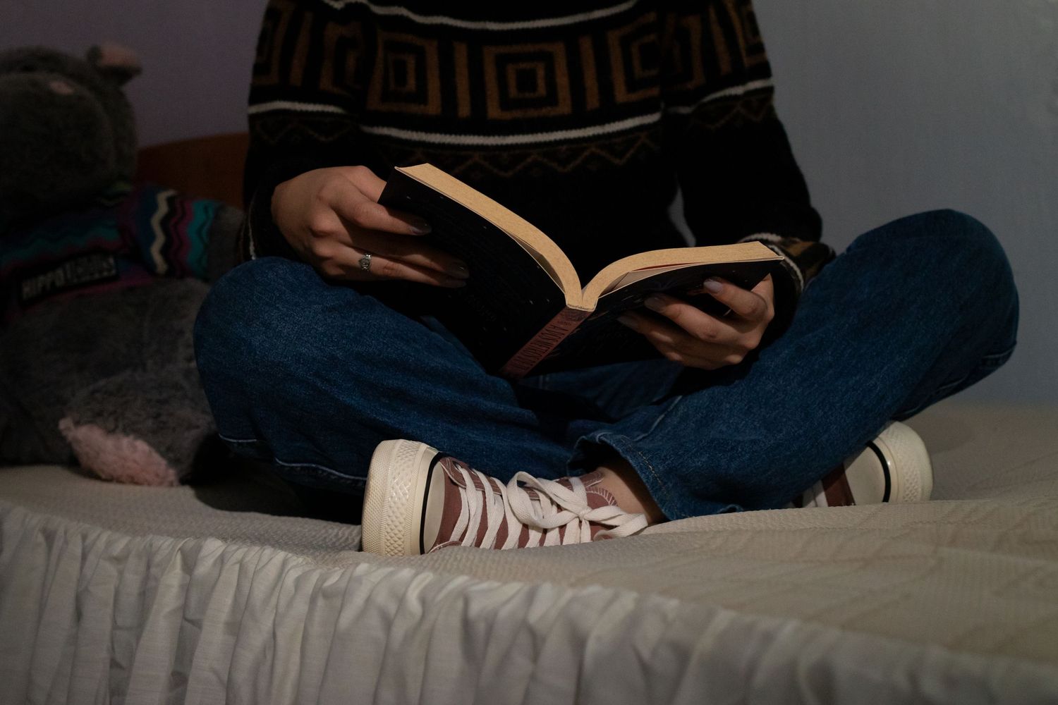 Person in dark clothing reading a book while lying down in a dimly lit room.