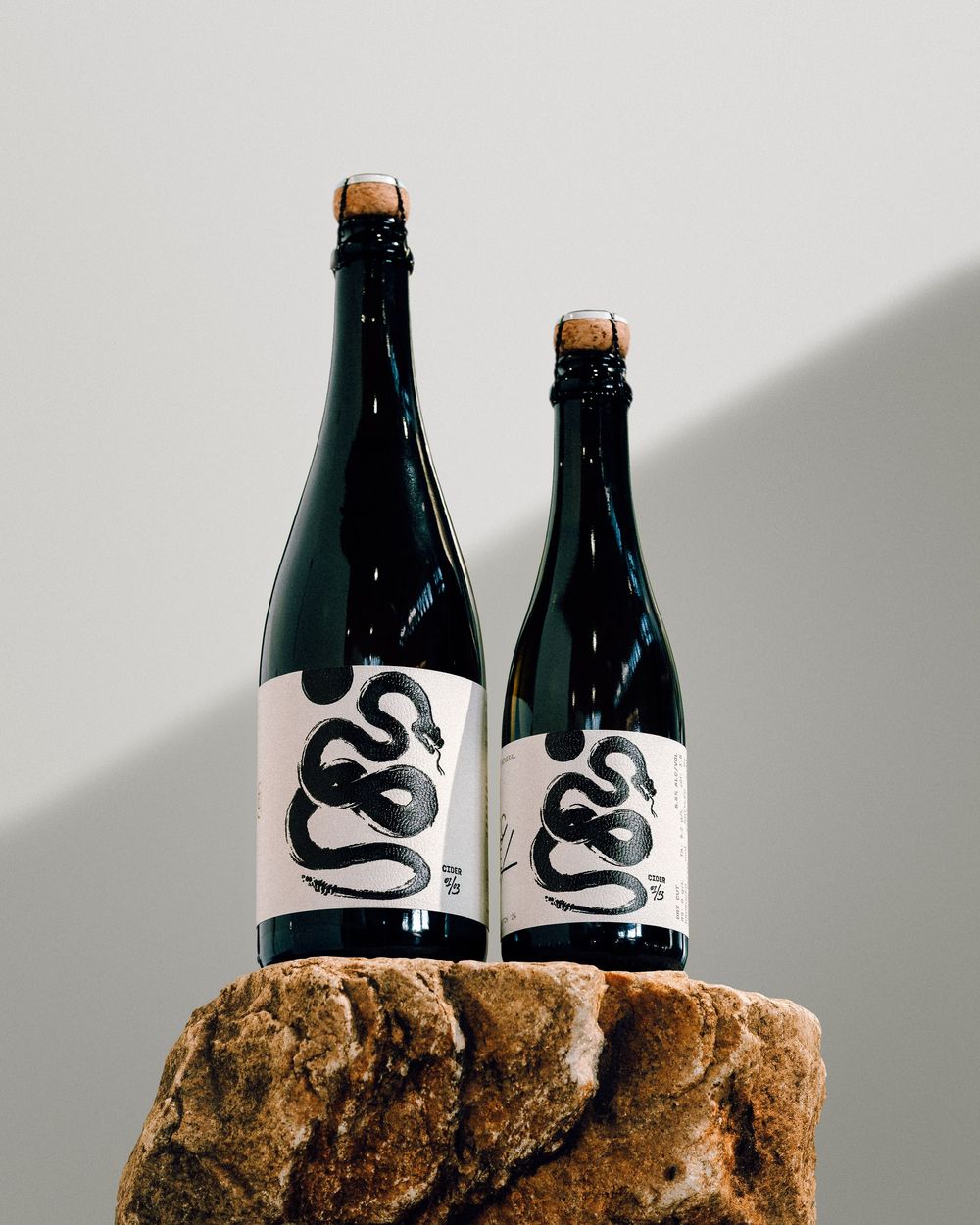 Two dark glass bottles with black and white snake design labels displayed on a textured stone surface.