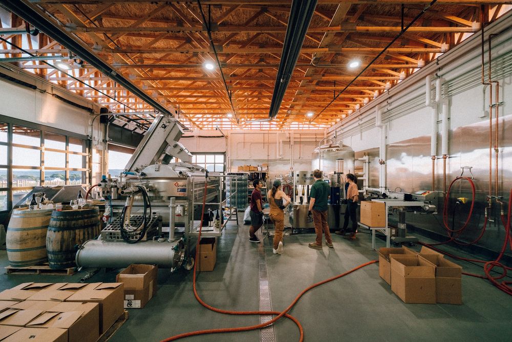 Large industrial manufacturing facility interior with wooden ceiling beams, equipment and storage areas visible throughout.