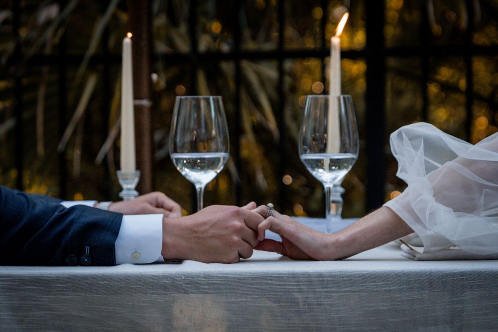 Bride and groom hold hands at candlelit wedding reception table with elegant wine glasses.