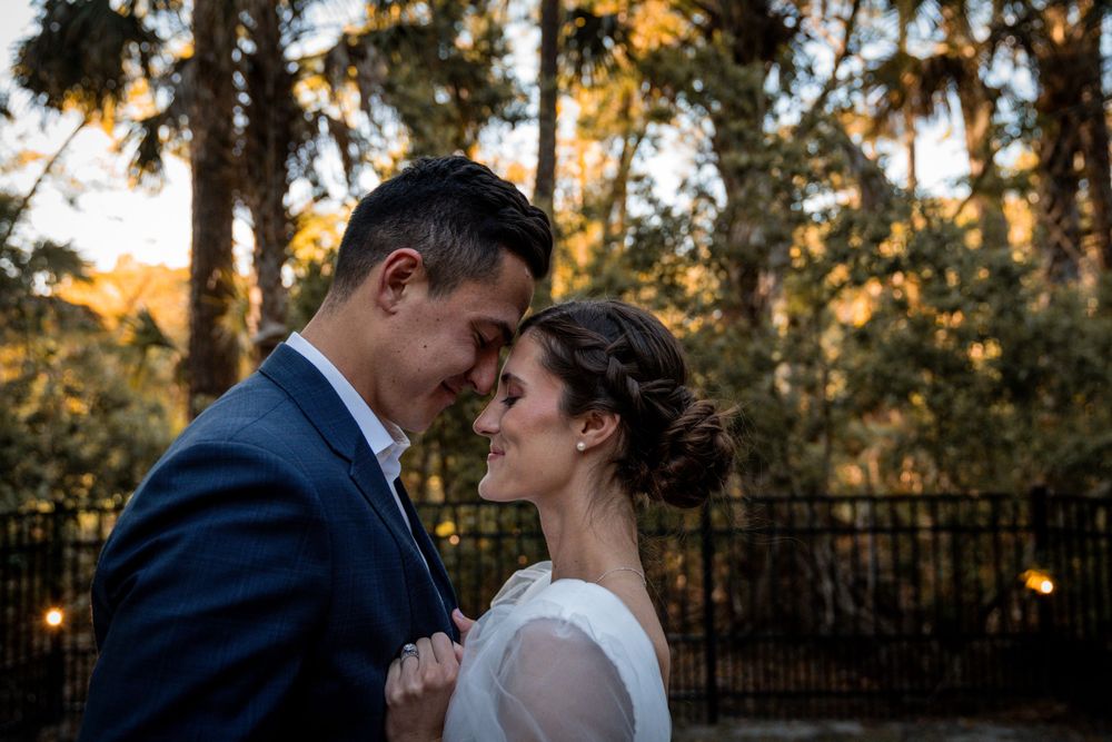 Bride and groom share intimate moment outdoors at golden hour among lush trees.