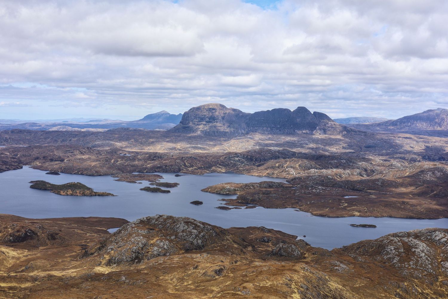 Panoramic view of Scottish Highland mountains with scattered lakes and islands.
