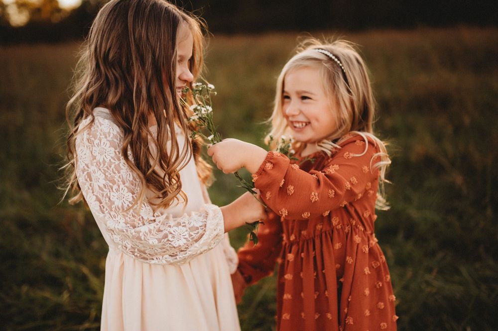 Two children in white lace and rust-colored dresses play together outdoors during golden hour.