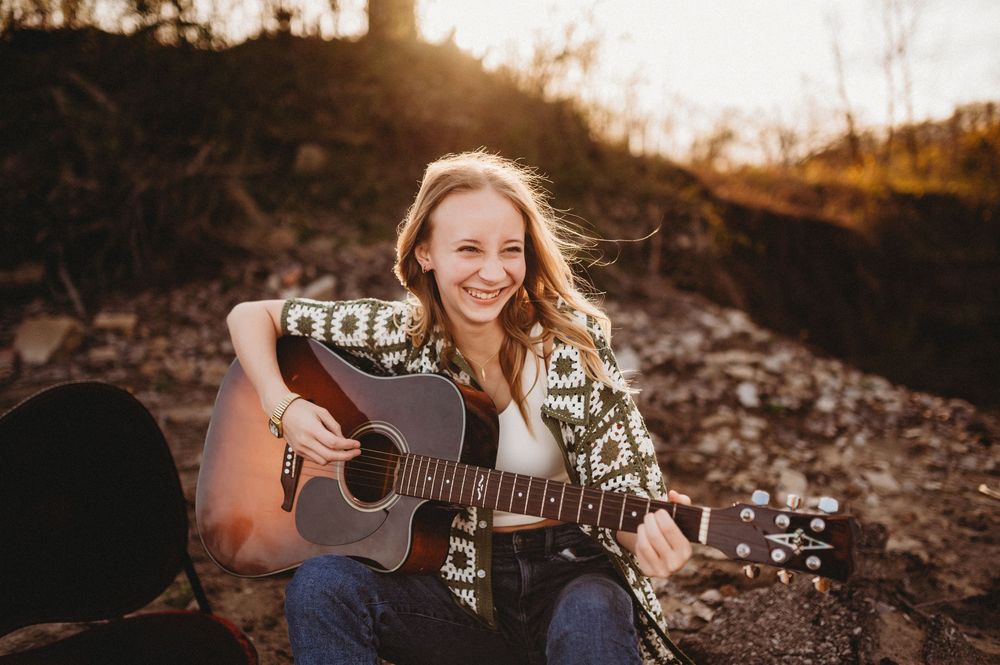 Person playing acoustic guitar outdoors during golden hour sunset in rocky terrain.