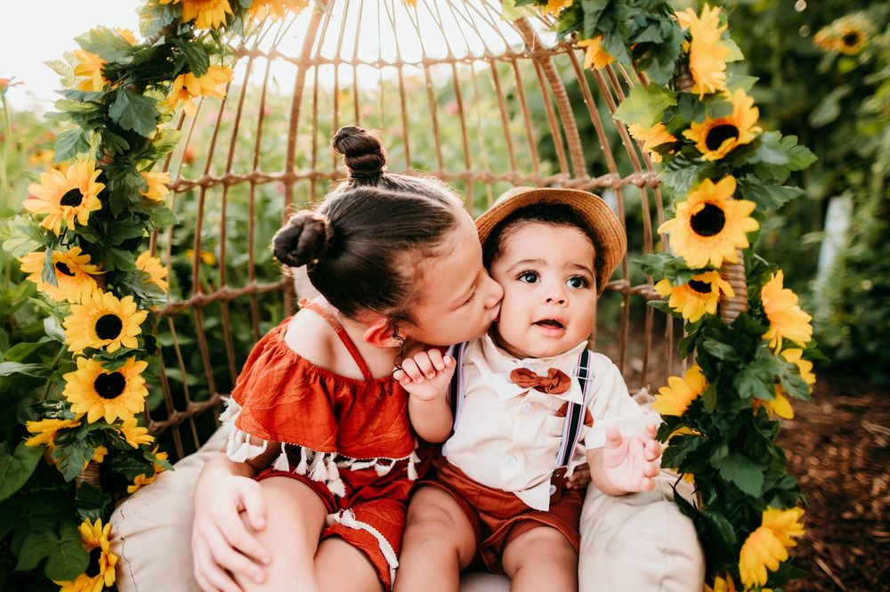 Two people embrace surrounded by bright yellow sunflowers and a decorative birdcage in an autumn garden setting.
