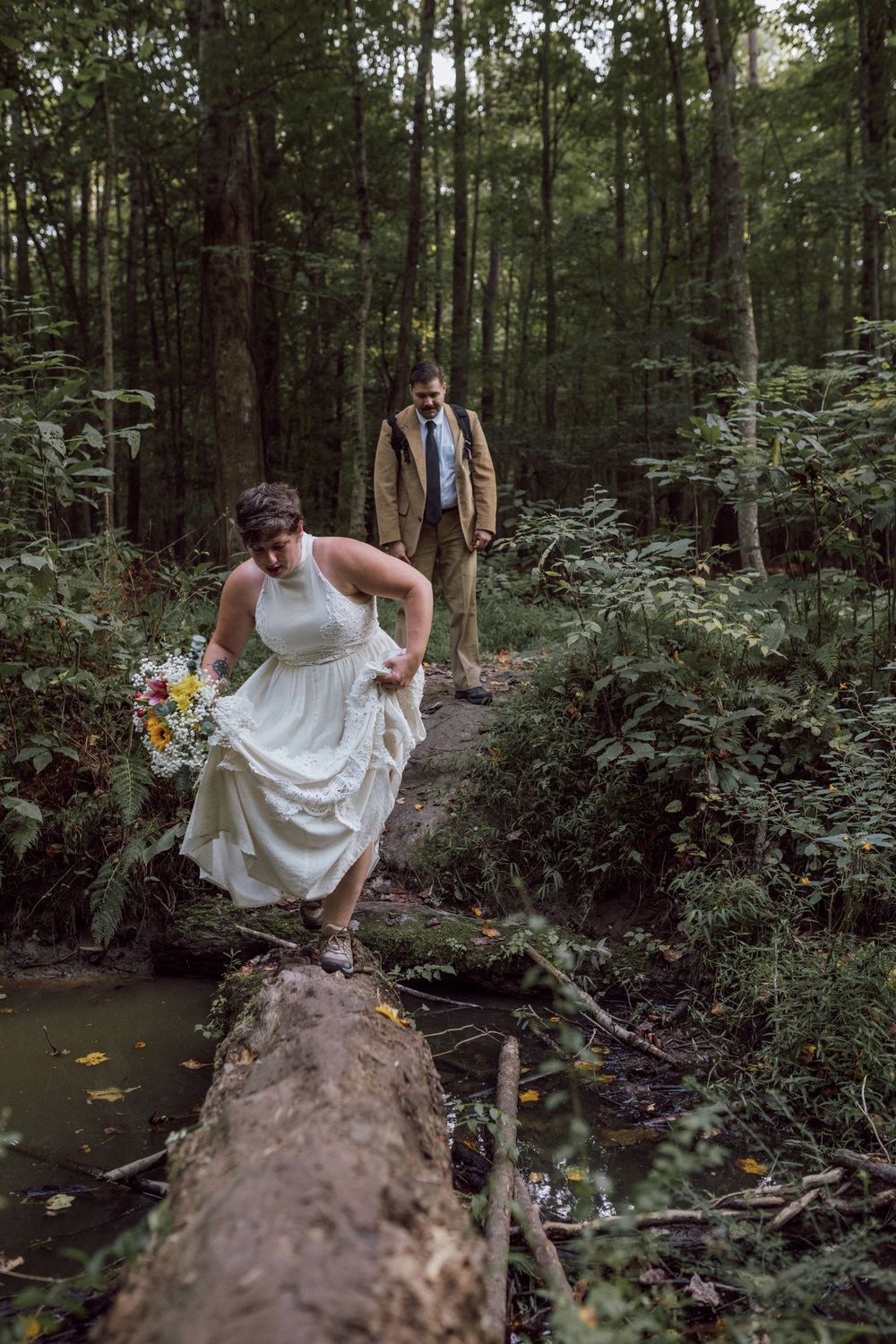 bride and groom hiking to elopement and crossing a log in virginia