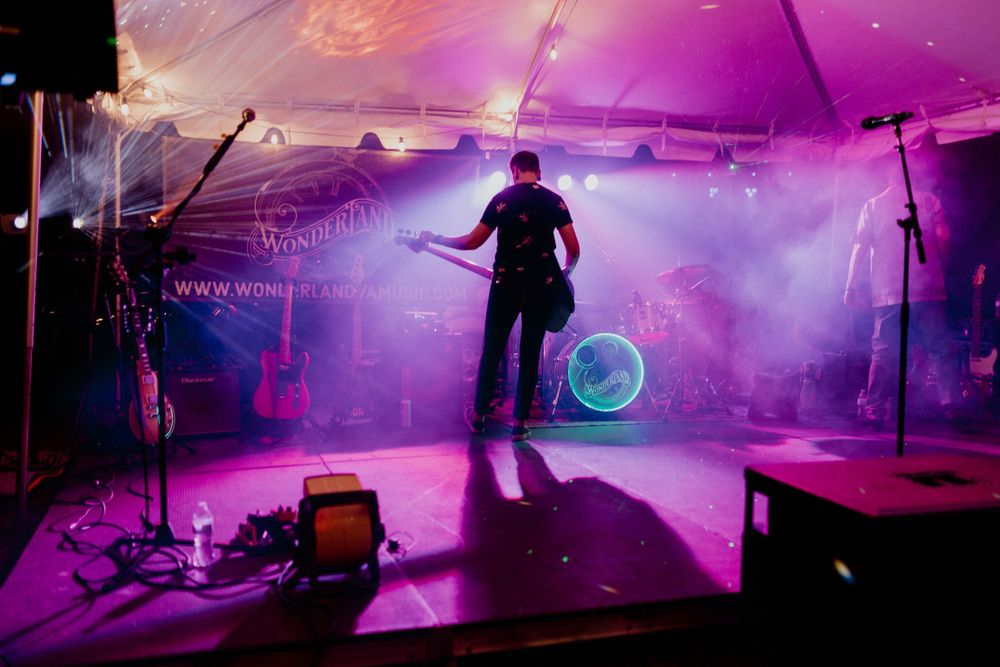 Silhouette of a performer on stage bathed in dramatic purple lighting with musical equipment and fog effects. wonderland chesapeake, va