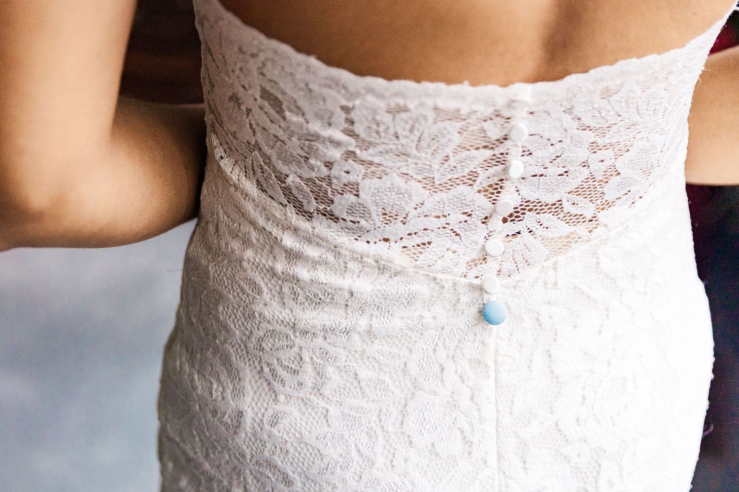 Close-up detail of delicate white lace wedding dress with blue embellishment.