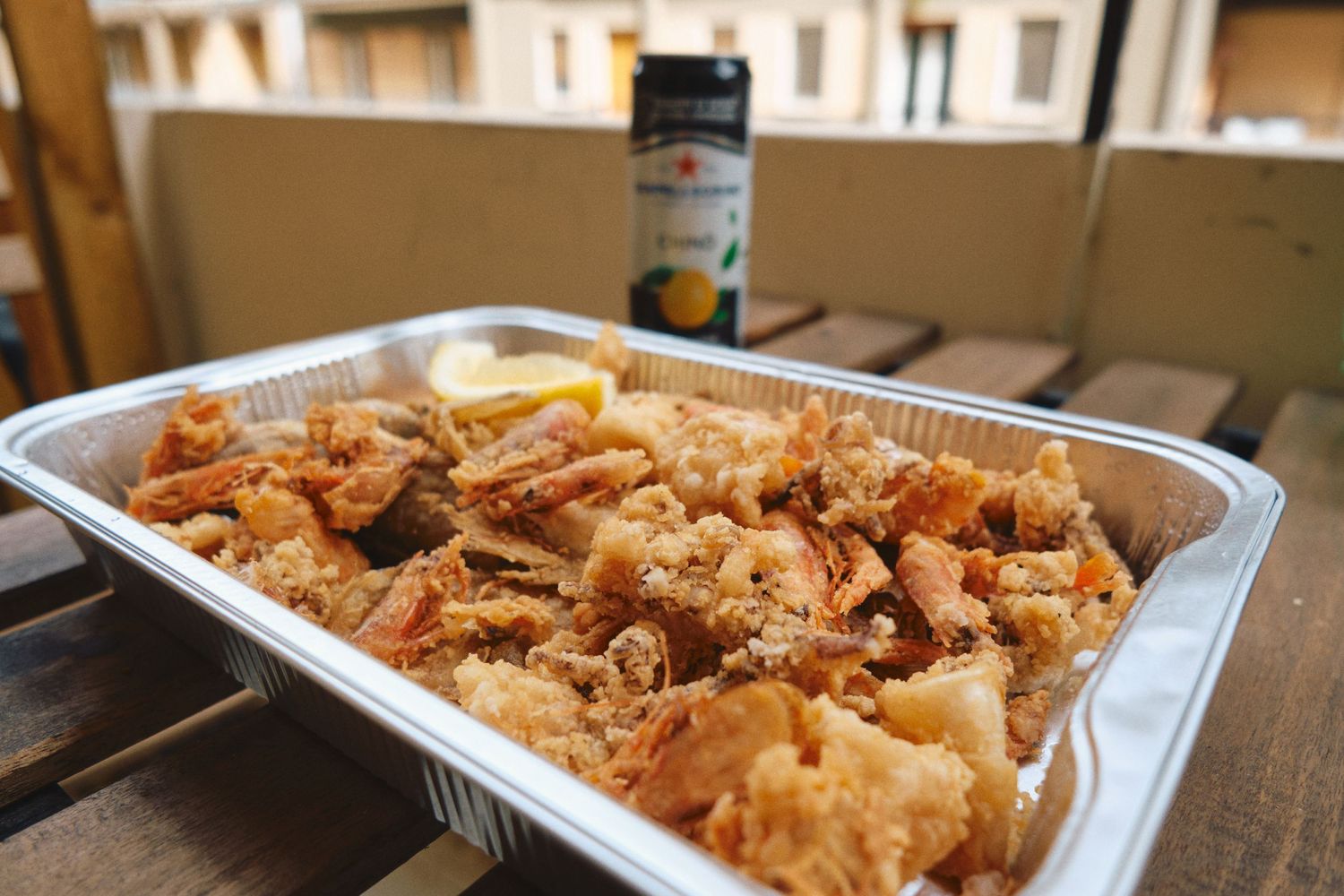Fried calamari and seafood served in a white takeout container on wooden table.