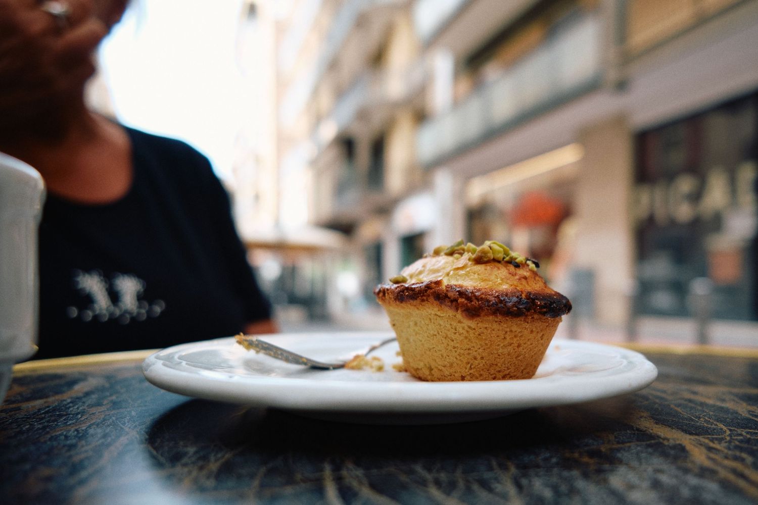 Close-up of a fresh muffin served on white plate at outdoor cafe table.