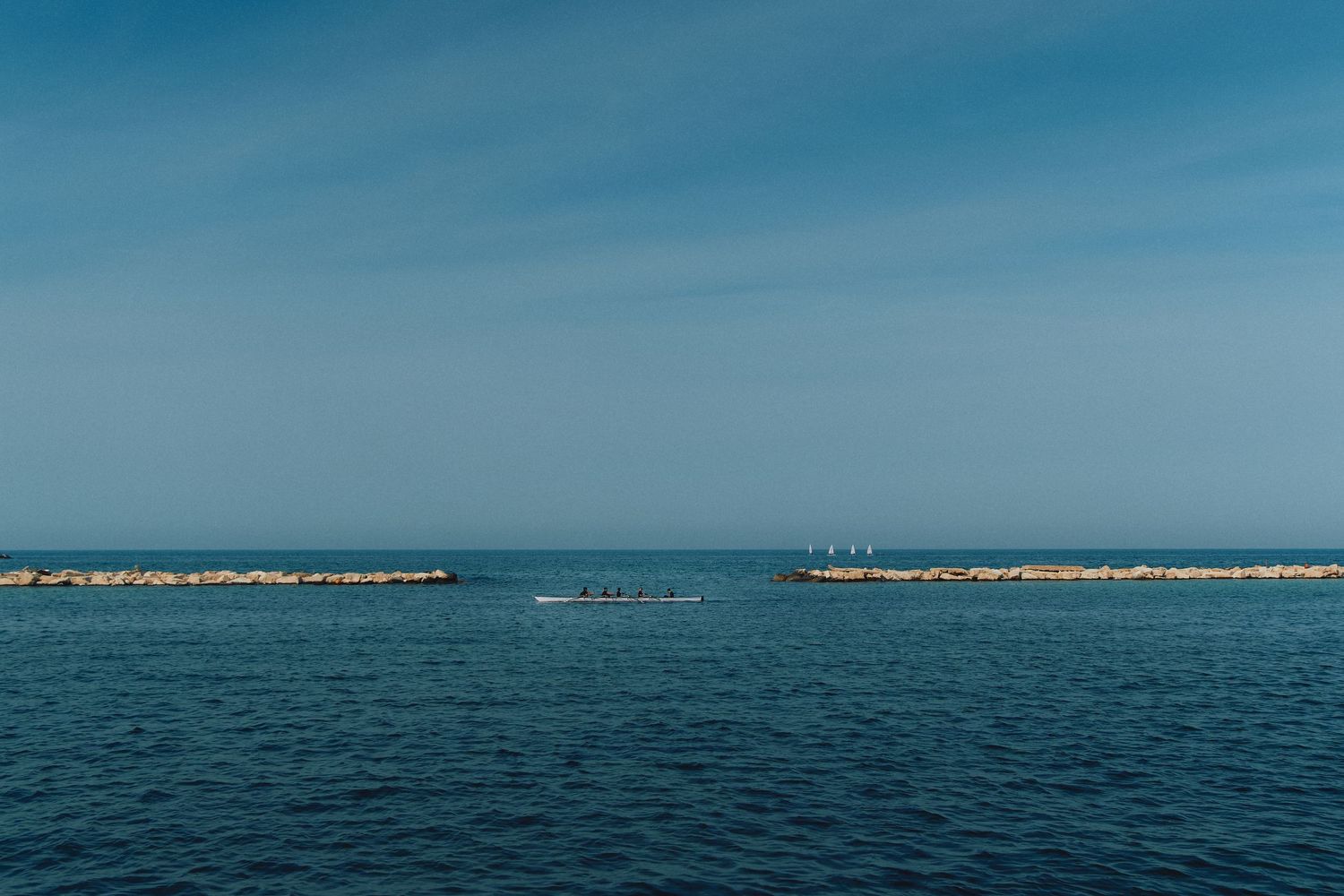 Serene seascape with rocky breakwaters extending into calm blue Mediterranean waters.