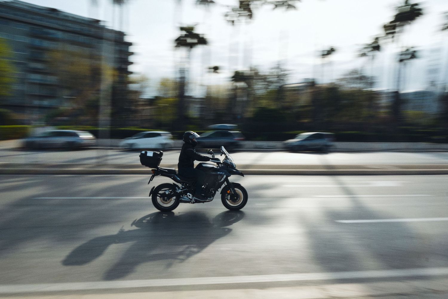 Motion-blurred motorcycle speeding down urban street with trees in background.